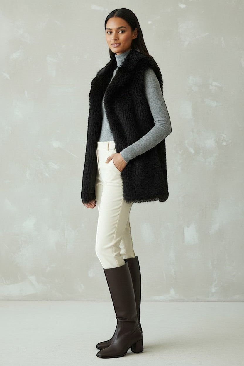 Refined Elegance black faux fur sleeveless vest worn by a model with a grey turtleneck, white trousers, and boots.