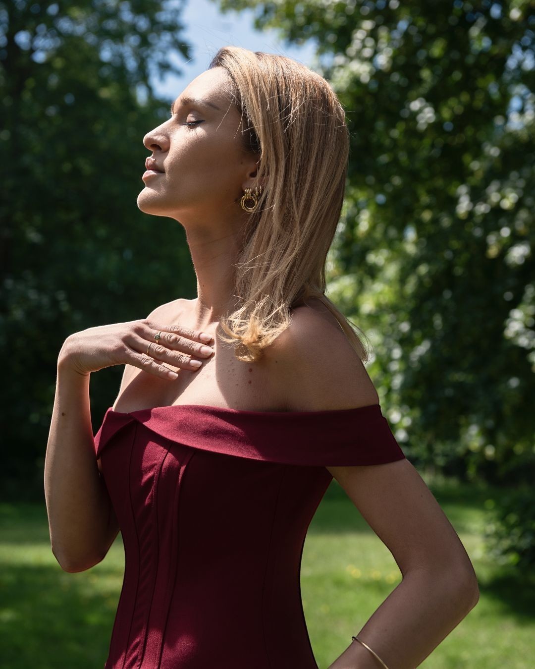 Refined Elegance Burgundy corset mini dress in deep red with an off-shoulder neckline worn by a woman in a garden
